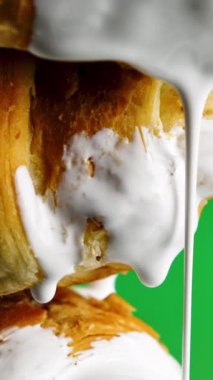 Beyaz kremalı şekerler. Borsa klipsi. Pişirme üzerine beyaz sıvı damlatıyor. Sıvı damlayan kremayla pişirme. Yeşil arka planda kremalı çöreğin yakın çekimi.