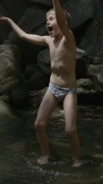 Yolculuktaki bir çocuk. Yaratıcı. Suda oynayan külot giymiş küçük bir çocuk ve uçurumdan gelen büyük kayalar arkadan görülebiliyor. Yüksek kalite 4k görüntü