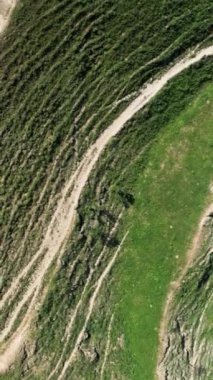 İlkbaharda Slovenya 'daki ulusal parktaki bir dağın havadan görünüşü. Başla. Yeşil çimlerle kaplı bir yamaçla yüksek bir tepenin üzerinde uçuyor ve dar yollar ve taşlarla ve kumla kaplı başka bir yokuş.