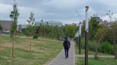 İnsanlar yaz günü fenerlerle parkta yürürler. Şarjör. Şehirdeki park yolu boyunca yürü. Yollu yeşil sokak ve şehrin arka planında yürüyen insanlar..