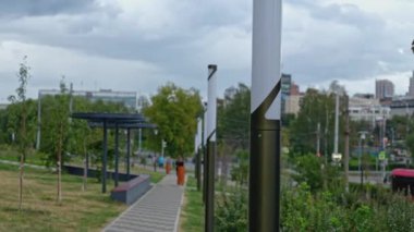 İnsanlar yaz günü fenerlerle parkta yürürler. Şarjör. Şehirdeki park yolu boyunca yürü. Yollu yeşil sokak ve şehrin arka planında yürüyen insanlar..