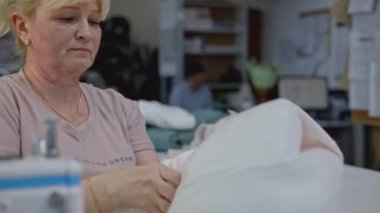 Dikiş üretimi, endüstriyel arka plan. Medya. Kadın ön tarafta yastık kılıfını çeviriyor.