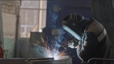 Fabrikadaki metal yapıları kaynaklıyor. Borsa klipsi. Maskeli kaynakçı metal yapıların montajı üzerinde çalışıyor. Sanayi tesislerinde kaynakçılık yapan profesyonel bir işçi.. 