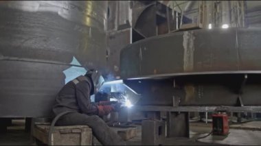 Büyük metal parçalarıyla endüstriyel fabrikada kaynakçı. Borsa klipsi. Kaynakçı elle büyük metal parçaları birleştirir. Makine fabrikasında kaynakçı ile endüstriyel kısım. 