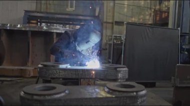 Büyük metal parçalarıyla endüstriyel fabrikada kaynakçı. Borsa klipsi. Kaynakçı elle büyük metal parçaları birleştirir. Makine fabrikasında kaynakçı ile endüstriyel kısım. 