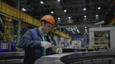 İşçi fabrikadaki yapısal parçaları ölçer. Borsa klipsi. Fabrikadaki miğferli işçiler parçaların ölçümlerini yapar. Genç adam fabrikada çalışıyor ve tasarım taş yapısını ölçüyor.. 