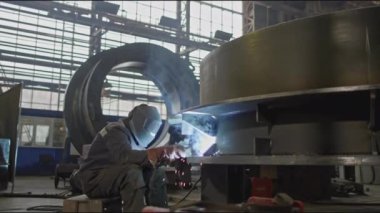 Büyük metal parçalarıyla endüstriyel fabrikada kaynakçı. Borsa klipsi. Kaynakçı elle büyük metal parçaları birleştirir. Makine fabrikasında kaynakçı ile endüstriyel kısım. 