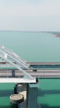 Turkuaz denizin havadan nefes kesen manzarası ve hakiki şekilli uzun beyaz bir köprü. Vuruldu. Mavi denizi ya da okyanusu geçen köprü boyunca giden nakliye aracı