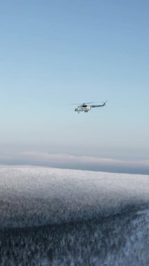 Mavi bir arka planda, karla kaplı ormanın üzerinde uçan bir helikopter. Şarjör. Doğal soğuk kış arkaplanı