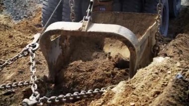 Kumlu toprağı kazan kazıcının detaylı bir yakın görüntüsü yoğun inşaat çalışmalarını vurguluyor.