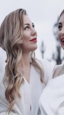 Dışarıda poz veren kırmızı dudaklı iki güzel sarışın kadın. Başla. Beyaz elbiseli yetişkin kadınlar tüylerden yapılmış bir şapka tutuyorlar, moda anlayışı.