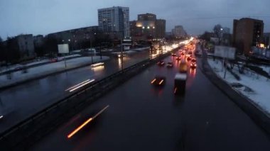 Akşam saatlerinde çekilen hareketli bir şehir yolu sahnesi. Arabalar hareket halinde ve şehir ışıkları manzarayı aydınlatıyor. Menkul Kıymetler