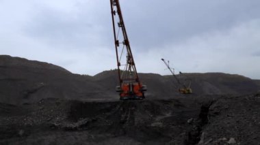 Kasvetli ve bulutlu gökyüzüyle karakterize edilmiş engebeli bir madencilik ortamında operasyonel ağır ekipman fonksiyonları. Menkul Kıymetler