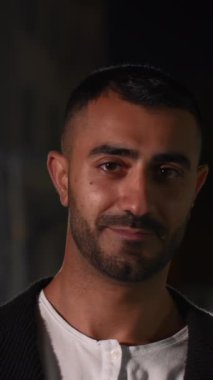 Yakışıklı bir adamın, kameraya bakıp flört edişinin portresi. Medya. Arka planda karanlık bir sokak olan bir adam avluda dikiliyor.