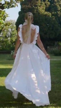 Güneşli bir yaz parkında genç ve güzel bir gelin. Başla. Küçük çalıları olan beyaz elbiseli bir kadın.