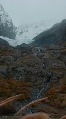 Ağaçlarla kaplı kocaman dağlar. Yaratıcı. Dağları ve taşların arasından akan ince nehirleri olan soğuk bir manzaranın kuş bakışı görüntüsü. Yüksek kalite 4k görüntü