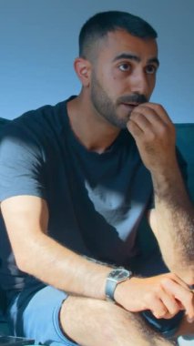 Genç adam TV 'de coşkuyla futbol izliyor. Medya. Adam duygusal olarak televizyonda futbol maçı izliyor. Adam abur cubur yiyor ve neşeyle futbol seyrediyor..