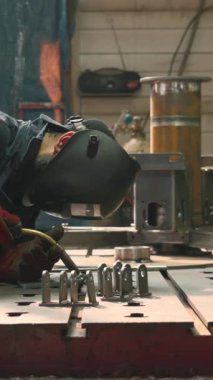 Koruyucu maskeli ve takım elbiseli profesyonel ağır endüstri işçisi fabrikada metal yapımında çalışıyor. Yaratıcı. Çelik ve demir kaynaklama şantiyesi, kıvılcımlı kaynak makinesi ve