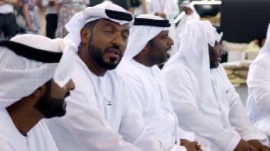 Dubai, BAE - Haziran 2024: Geleneksel kıyafetlerini giymiş Emirati erkekleri canlı bir kültürel etkinlikte aktif olarak diyalog içine giriyorlar. Medya