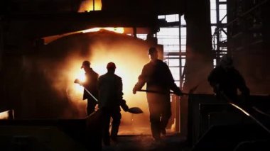 Siluetli işçiler, arka planda yoğun bir şekilde parlayan erimiş metalle, hareketli bir çelik fabrikasında özenle çalışıyorlar. Menkul Kıymetler
