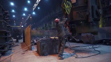 Çalışkan bir işçi, loş aydınlatılmış çelik fabrikasında, karmaşık endüstriyel süreçleri gösteren makineleri ustalıkla çalıştırır. Menkul Kıymetler