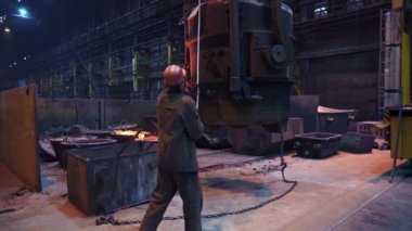 Bir işçi, yoğun bir metal fabrikası ortamında ağır makineleri özenle yönetir ve çalıştırır. Menkul Kıymetler