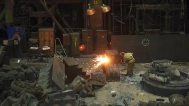 Kendini adamış bir işçi yoğun bir dökümhanede ağır makineler ve çeşitli aletlerle çevrili iken erimiş metal döküyor. Menkul Kıymetler