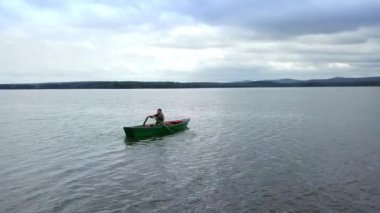 Yalnız bir kanocu, bulutlu bir gökyüzünün altındaki manzaranın tadını çıkararak sakin ve pürüzsüz bir gölde yavaşça kürek çekiyor. Menkul Kıymetler