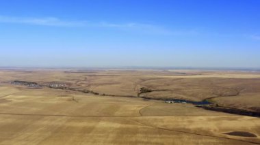 Uçsuz bucaksız altın tarlaların ve berrak mavi gökyüzünün altında sakin bir nehrin çarpıcı hava manzarasını deneyimleyin. Menkul Kıymetler