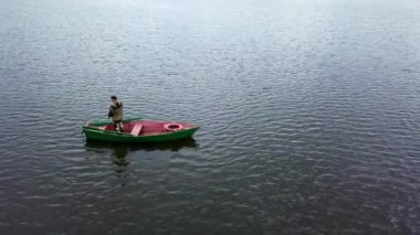 Yalnız bir balıkçı yeşil bir teknede sessizce duruyor, sakin ve parıldayan sularda huzur içinde yüzüyor. Menkul Kıymetler