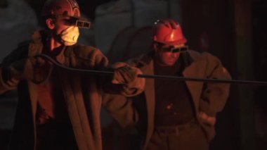 Metal bir çalışma ortamında, iki kendini adamış işçi koruyucu ekipman ustalıkla ağır makineler kullanıyor. Menkul Kıymetler