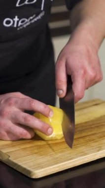 Ahşap bir tahtada taze soyulmuş portakal kesen bir erkek şefin yakın çekimi. - Sanat. Vejetaryen yemeği, vitamin ve yemek yapma kavramı.
