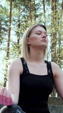 Doğaya derinden bağlı mutlu kadın ormanda meditasyon ve birlik hissediyor. Kavram. Spor takım elbiseli sarışın kız yaz günü meditasyonda beton merdivenlerde oturuyor.