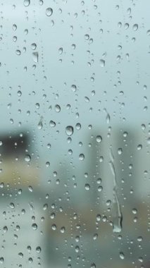 Yağmurlu bir günde camlı pencereyi kapatın. Bulanık şehrin arka planında büyük damlalar olsun. Stok görüntüleri. Dikey cam yüzeyde saydam su damlaları.