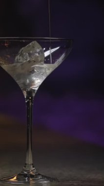Martini bardağına buz küpüyle alkol dök. Stok görüntüleri. Kalın alkollü içecek koyu arkaplandaki şeffaf camlara dökülüyor..
