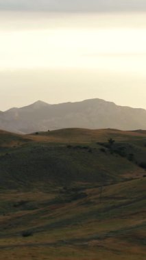 Büyük yeşil tepelerin, patikaların ve arka planda dağ zinciri olan küçük çalılıkların hava manzarası. İnanılmaz renkli bir manzara.