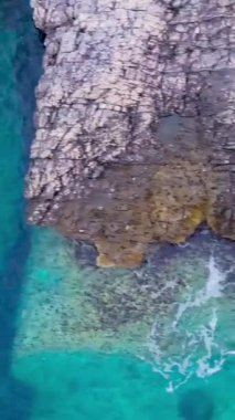 Mavi sahilin kayalıklı üst manzarası. Hisse. Cennet lagünündeki gibi turkuaz suyu olan kayalık bir sahil. Turkuaz dalgalar kayalık sahilde suyun altında derin çöküntülerle kırılır.