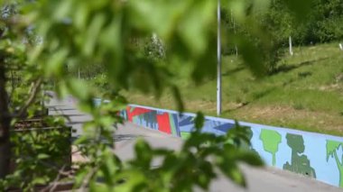 Yeşillik tarafından çerçevelenmiş, manzaralı bir yol boyunca canlı bir duvar resmi, çarpıcı kentsel sanat özellikleri sergiliyor. Kırp
