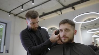 Şık ve çağdaş bir salon ortamında, çok yetenekli bir berber müşterinin saçını ustalıkla buduyor. Kırp
