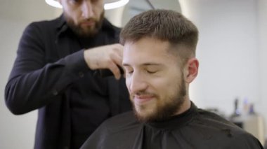 Son derece yetenekli bir berber, modaya uygun bir salon ortamında tamamen rahat bir müşterisine ustalıkla yeni bir saç kesimi yapıyor. Kırp