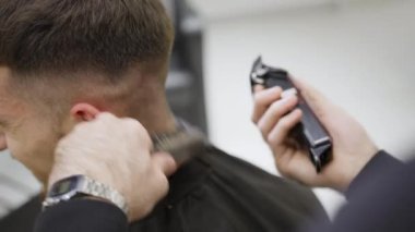 Çağdaş bir kuaför ortamında, yetenekli bir berber titizlikle hassas aletler kullanarak şık bir saç kesimi yapıyor. Kırp