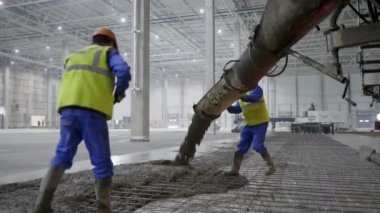 Yetenekli işçiler inşaat halindeki büyük bir deponun zeminine titizlikle beton döküyorlar. Kırp