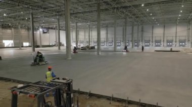 Yetenekli işçiler, geniş bir sanayi deposunun beton zeminini ustalıkla döşeyip bitiriyorlar. Kırp