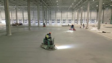 İşçiler, çok geniş bir endüstriyel tesisin döşemesini etkin bir şekilde bitirmek için makineler kullanıyorlar. Kırp
