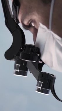 Profesyonel gözlüklü bir cerrah. Dürbünlü gözlüklü bir doktorun yan görüntüsü laboratuvarda bir şeyi inceliyor..