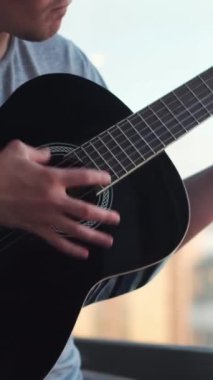 Yalnız adamın açık bir pencereye gitar çalmasına yakın çekim. Genç müzisyen klasik akustik gitarda akorlar ve şarkılar çalıyor..