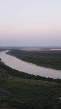 Küçük bir köyü, ormanı ve nehri olan yaz kırsal arazisi, hava manzarası. Bereketli yeşil çayırlar ve tarım arazileri olan doğal manzara, gün batımında bir nehir ve bir köy..