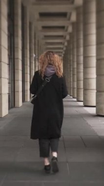 Sırtı kameraya dönmüş, sütunların arasında yürüyen bir kız. Kıvırcık saçlı bir kadının, büyük pencereleri ve kocaman sütunları olan binanın yakınlarında yürüdüğünü gördüm..