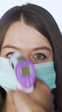 Maskeli kadın AVM 'de sıcaklığı kontrol ediliyor. Medya. Sinema ve alışveriş merkezlerini ziyaret edenler temas olmayan termometre kullanılarak sıcaklık için kontrol edilirler..
