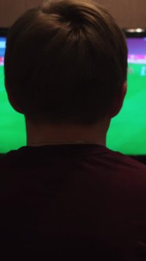 Genç adam evde televizyondan futbol maçı izliyor. Evdeki kanepede oturan ve gece geç saatlerde futbol izleyen bir adamın arka görüntüsü..